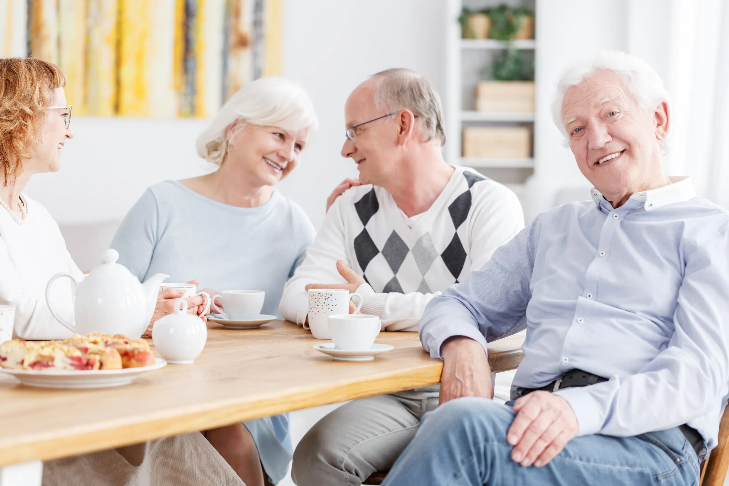 Happy elderly people spending time together at nursing home, senior man smiling at camera with friends chatting in the background